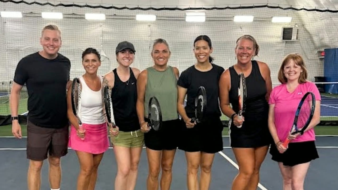 Will Gross with six women players holding their racquets on an indoor court